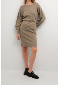 Maglione beige a maglia con spalle rilassate e maniche lunghe abbinato a una gonna beige aderente e scarpe in pelle nera.