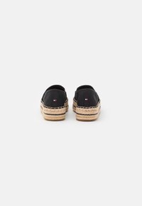 Espadrilles de lona negra con suelas de yute, que presentan una superficie texturizada y un panel elástico en la parte trasera, acentuadas por un pequeño detalle de logo.