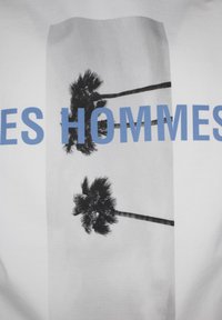 Weißes T-Shirt mit einem schwarz-weißen Grafikmotiv von Palmen und dem Text "LES HOMMES" in Blau, zentral auf dem Stoff platziert.