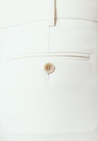 Białe spodni o dopasowanym kroju wykonane są z gładkiego, strukturalnego materiału, z jedną tylną kieszenią, zamykaną okrągłym, jasnym guzikiem.