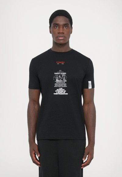 Black cotton t-shirt features a graphic print with white text and illustrations. Includes an orange logo at the neckline and a side label.