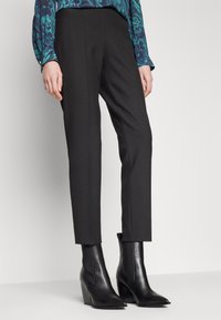 Svarta skräddarsydda byxor med smal passform, med en slät textur och rena linjer, matchade med svarta klackade ankelstövlar.