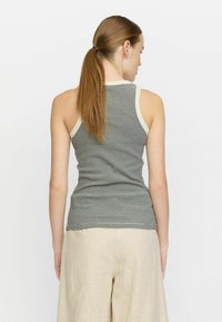 Top sin mangas a rayas en verde y crema, hecho de una tela elástica. Presenta un escote redondeado y un ajuste ceñido, acompañado de pantalones sueltos color beige.