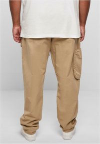 Beige cargo pants with a relaxed fit, featuring a side pocket and a smooth texture. Paired with a plain white t-shirt and white sneakers.