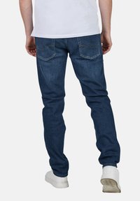 Jeans de mezclilla azul oscuro con un corte ajustado, bolsillos traseros con detalles de costura, combinados con zapatillas blancas.