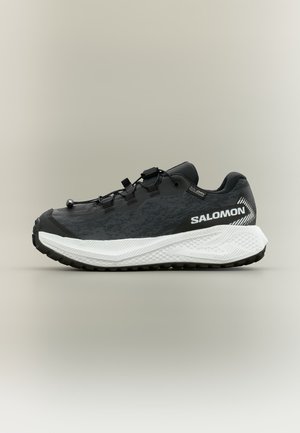 Black and white Salomon running shoe with thick textured sole and quick lace system, shown from the side on a plain background.