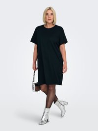 Black oversized t-shirt dress with short sleeves, paired with silver metallic ankle boots and a matching small handbag, against a light background.