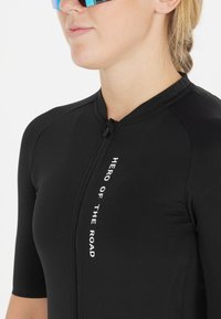 Schwarzes Fahrradtrikot mit kurzen Ärmeln, ausgestattet mit einem Reißverschluss vorne und dem Text "HERO OF THE ROAD" in Weiß. Glatte, elastische Stofftextur.