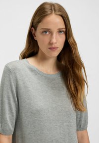 Light gray knit sweater with a round neckline, short sleeves, and a smooth texture. Features a subtle ribbed trim at edges.