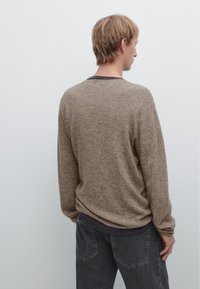 Brown knit sweater with a relaxed fit, featuring a crew neckline and ribbed texture. Paired with dark gray jeans.