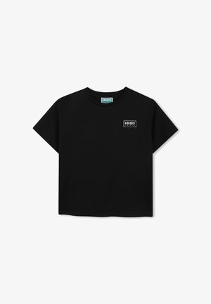 T-shirt noir à manches courtes et col rond avec un petit logo blanc "KENZO PARIS" sur le côté gauche de la poitrine et une étiquette verte à l'intérieur du col.