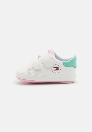 Zapatilla blanca para niño pequeño con suela rosa, parche verde en el talón, dos cierres de velcro y el logo de Tommy Hilfiger en el lateral.