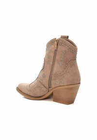 Botín de ante beige con cierre lateral, punta afilada y tacón apilado. Adornado con tachuelas plateadas en patrones de estrellas a lo largo de los lados.