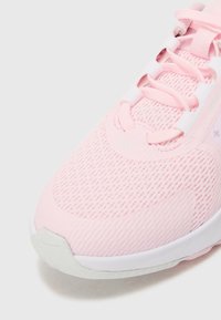 Lys rosa treningssko med mesh-overdel, teksturerte paneler og hvit såle. Snøring med ekstra forsterkningsdetaljer.