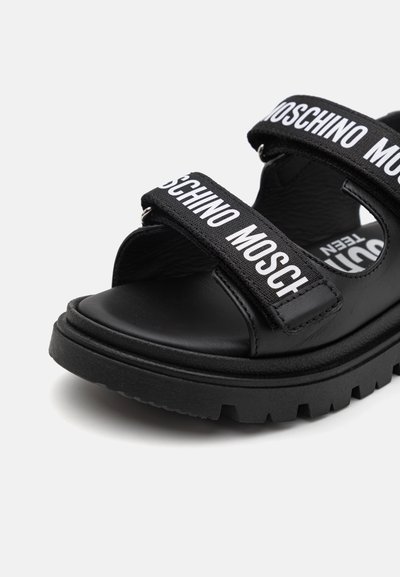 Sandalias negras con dos correas ajustables con la marca "Moschino", hechas de material sintético, con una suela texturizada y un diseño robusto.