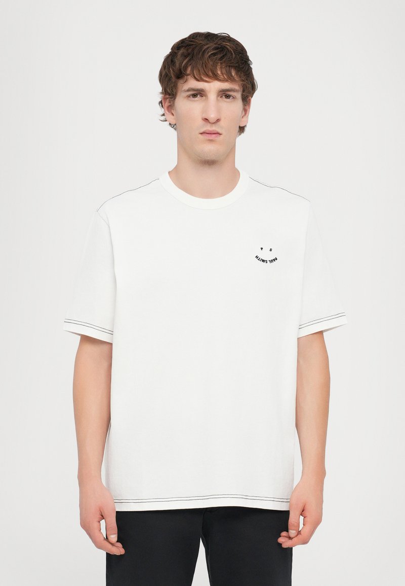White cotton t-shirt with short sleeves, featuring a small black smiley face design on the chest and contrasting stitching along the edges.