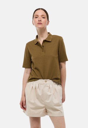 Polo brun à manches courtes, avec un col et trois boutons. Associé à un short plissé beige clair. Fond uni.