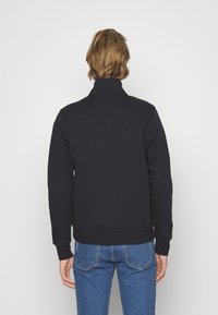 Felpa blu navy con colletto alto e polsini a coste, caratterizzata da una texture uniforme e un orlo cropped, indossata con jeans azzurri.