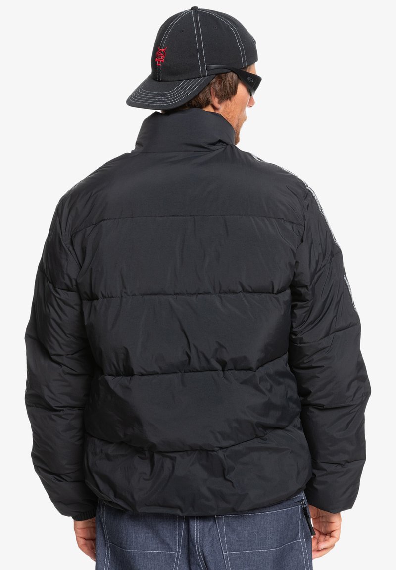 Czarna kurtka puchowa z wysokim kołnierzem, pikowanym wzorem i gładką fakturą. Z tyłu znajduje się detal z logo oraz odblaskowe akcenty po bokach.