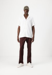 White short-sleeve button-up shirt, brown loose-fitting pants, and white sneakers. A green cap completes the outfit. Simple design.