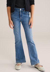 Hellblaue, aus Denim gefertigte Schlagjeans mit hoher Taille. Klassisches Fünf-Taschen-Design mit taillierter Passform, feinen Nähten und einem silbernen Knopf.