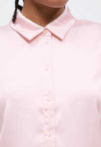 Blusa de cetim rosa claro com gola clássica e botões frontais; textura suave com brilho subtil.