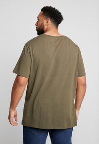 Olijfgroene katoenen t-shirt met korte mouwen, ontspannen pasvorm, ronde halslijn en platte zoom. Stijlvolle textuur, geen zichtbare patronen of accenten.
