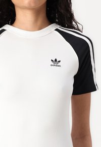 White and black short-sleeve T-shirt made of soft cotton with a round neck, featuring black shoulder panels and an embroidered Adidas logo.