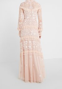 Lång, genomskinlig klänning i persikofärg med intrikata blommönster och paljetter. Hög hals, långa ärmar och lager av tyllkjol. Dragkedja bak.