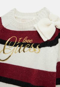 Suéter de punto a rayas en rojo, negro y blanco con texto en lentejuelas doradas que dice "Amo Guess". Presenta un cuello acanalado y un lazo decorativo en crema.