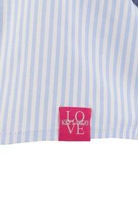 Tela de rayas verticales en azul claro y blanco con una pequeña etiqueta rosa que dice "LOVE KEY LARGO" cosida cerca del borde.