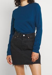 Long-sleeve teal top with a crew neck, paired with a black denim skirt featuring frayed hem and front pockets.