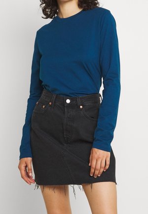 Haut teal à manches longues avec un col rond, associé à une jupe en denim noire avec un ourlet effiloché et des poches avant.