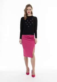 Schwarzer Langarmpullover mit Strassakzenten, kombiniert mit einem figurbetonten rosa Rock mit Raffung und einem seitlichen Schlitz. Rosa High Heels runden den Look ab.
