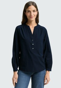 Blusa blu navy con scollo a V, pattina con bottoni e maniche lunghe con polsini elastici. Realizzata in tessuto testurizzato per un dettaglio in più.