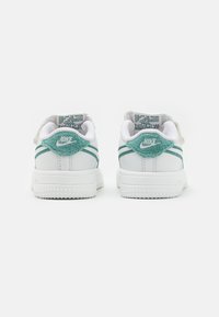 Baltos sportbačiai su žalia suede akcentais, turintys dvi žalias juosteles ant kulno ir tekstūruotą pados paviršių. Nike logotipas ant nugaros.