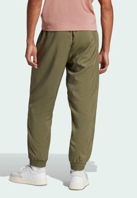 Olijfgroene joggingsbroek met een elastische tailleband en boorden, gemaakt van lichte stof, gecombineerd met witte sneakers.