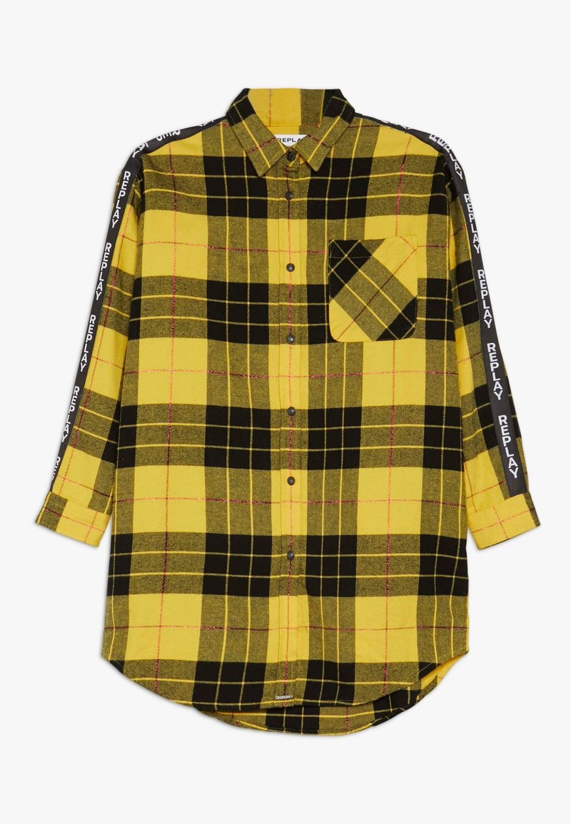 Chemise en flanelle à carreaux jaune et noir, manches longues, fermeture boutonnée, poche poitrine et accents noirs de marque sur les manches.