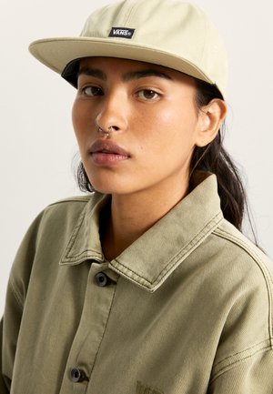 Jasnozielona czapka z czarną naszywką logo Vans, w połączeniu z pasującą oliwkową koszulą z guzikami, charakteryzującą się wytrzymałym materiałem i widocznymi szwami.