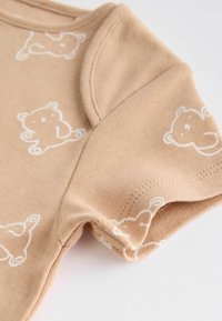 Beige bomullströja för spädbarn med korta ärmar, med tryck av vita björnar och rund halsringning. Slät textur och rena sömdetaljer.