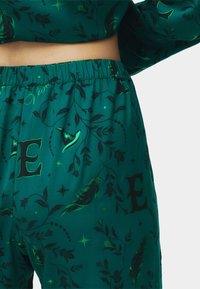 Pantalones de pijama verdes con un estampado floral y de letras, hechos de tela suave con una cinturilla elástica, y decorados con plumas y estrellas.