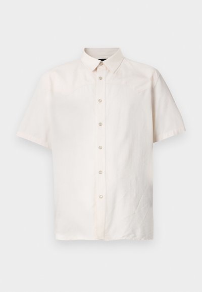 Lühikeste varrukatega särk heledast beežist kangast, millel on nööpidega esiosa, tagasihoidlik krae ja lihtsad õmblused külgedel.