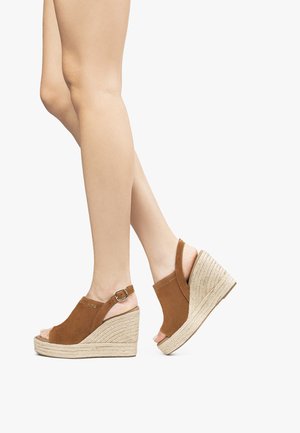 Sandales à talons en suede brun avec une semelle en jute, design à bout ouvert, et une sangle au niveau de la cheville avec une boucle en métal.