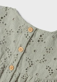 Abito in tessuto verde chiaro con un design in pizzo floreale e ritagli, rifinito con bottoni di legno sul corpino e gonna arricciata.