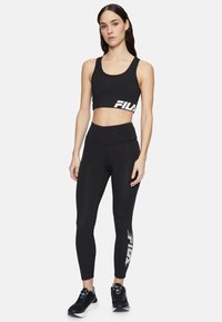 Svart atletisk crop top och högmidjade leggings från FILA, med en vit logotyp. Slät, elastisk tyg, figurnära design. Svarta atletiska skor.