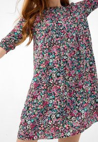 Blommig klänning med svart bas och rosa, blå och gröna blommor. Den har en rynkad halsringning och trekvarts långa ärmar med elastik.