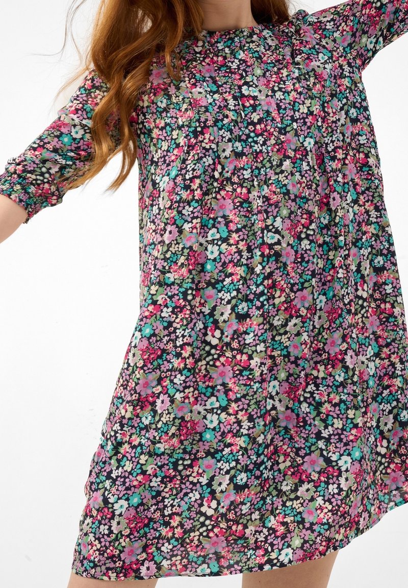 Blommig klänning med svart bas och rosa, blå och gröna blommor. Den har en rynkad halsringning och trekvarts långa ärmar med elastik.