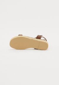 Brown leather sandal with a woven-patterned espadrille sole. Includes an adjustable ankle strap and a flat, rubber-like bottom.