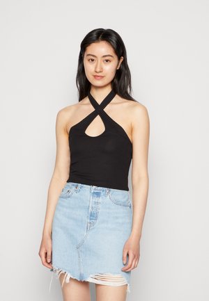 Top preto com decote halter e recorte em forma de olho-chave, com textura canelada. Combinado com uma saia de ganga azul clara com barra desfiada e detalhes desgastados.