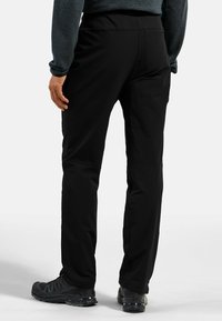 Schwarze Wanderhosen mit glatter Textur und elastischem Bund, ausgestattet mit Seitentaschen und einem schmal zulaufenden Bein. Getragen mit schwarzen Wanderschuhen.